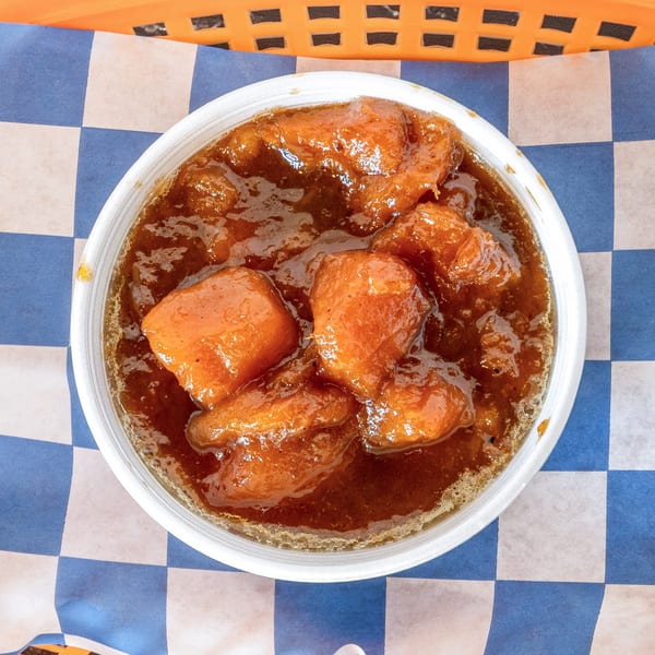 A white bowl of Suthern Cluck's candied yams in a rich brown sauce on blue and white checkered paper.