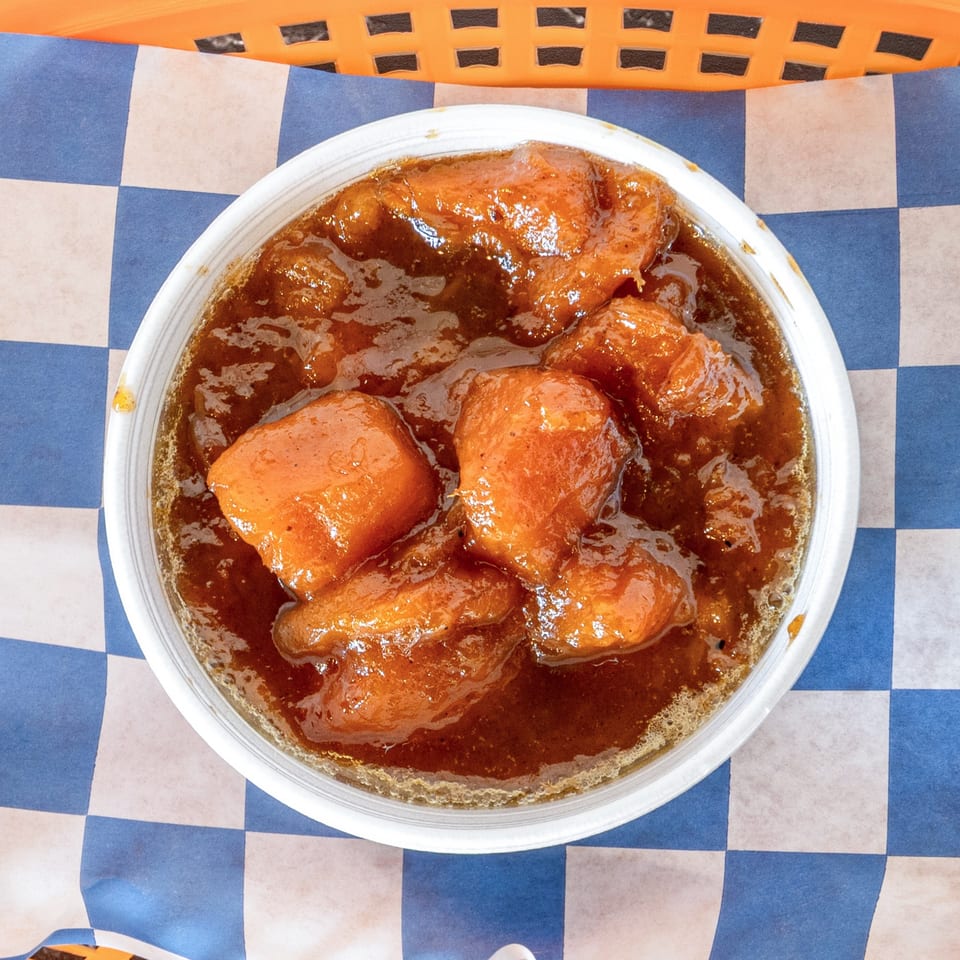 A white bowl of Suthern Cluck's candied yams in a rich brown sauce on blue and white checkered paper.