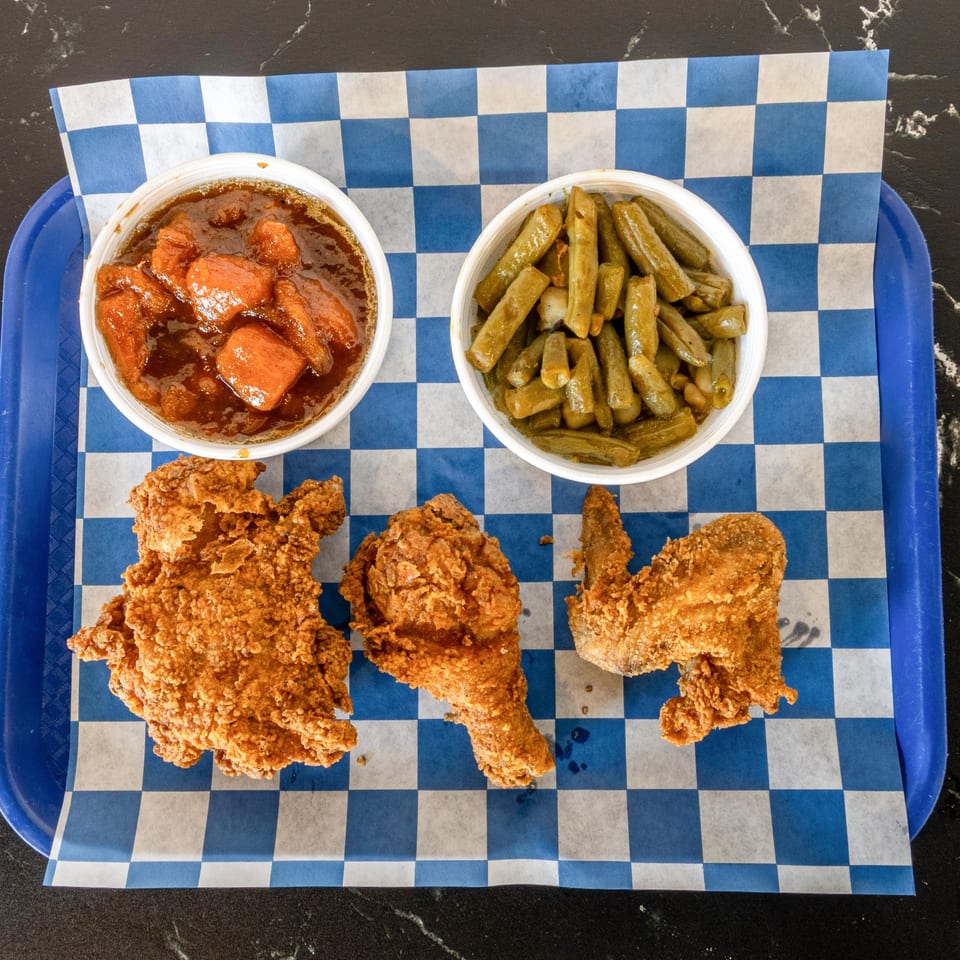 Suthern Cluck fried chicken pieces, candied yams, and green beans on a blue checkered tray liner.