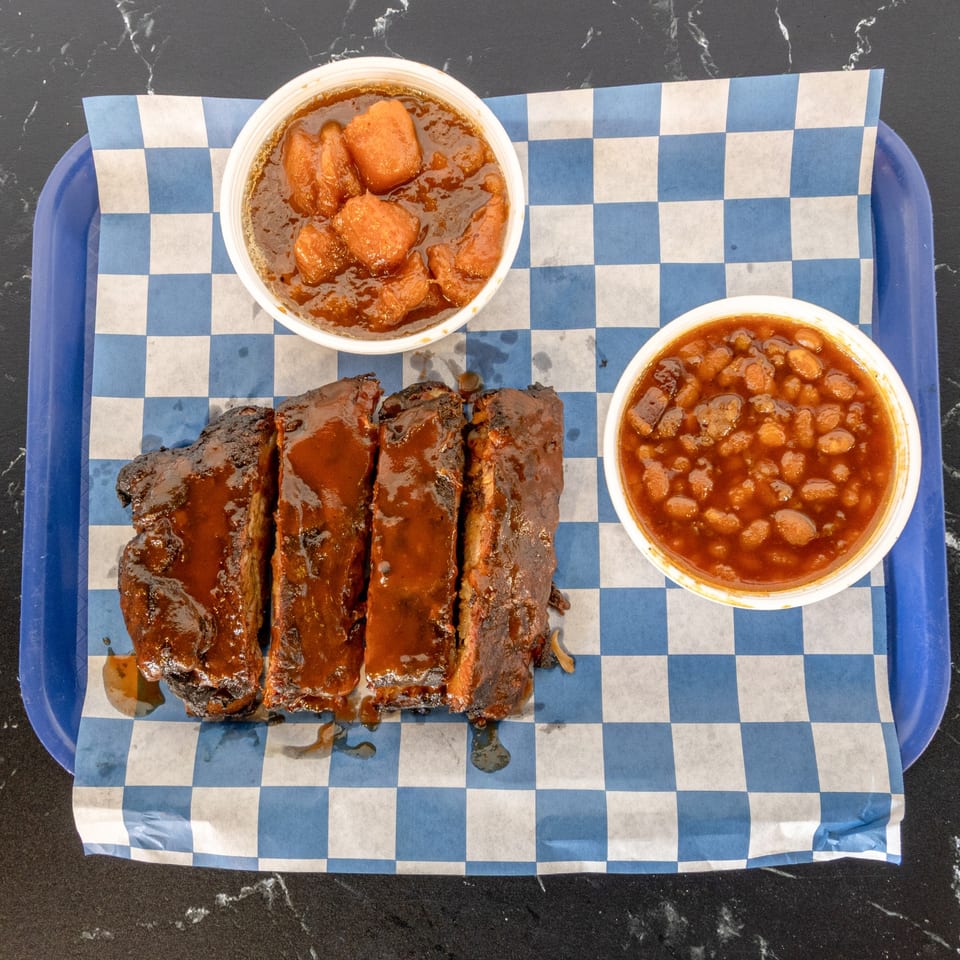 Suthern Cluck's BBQ ribs with baked beans and candied yams on a blue checkered tray liner.