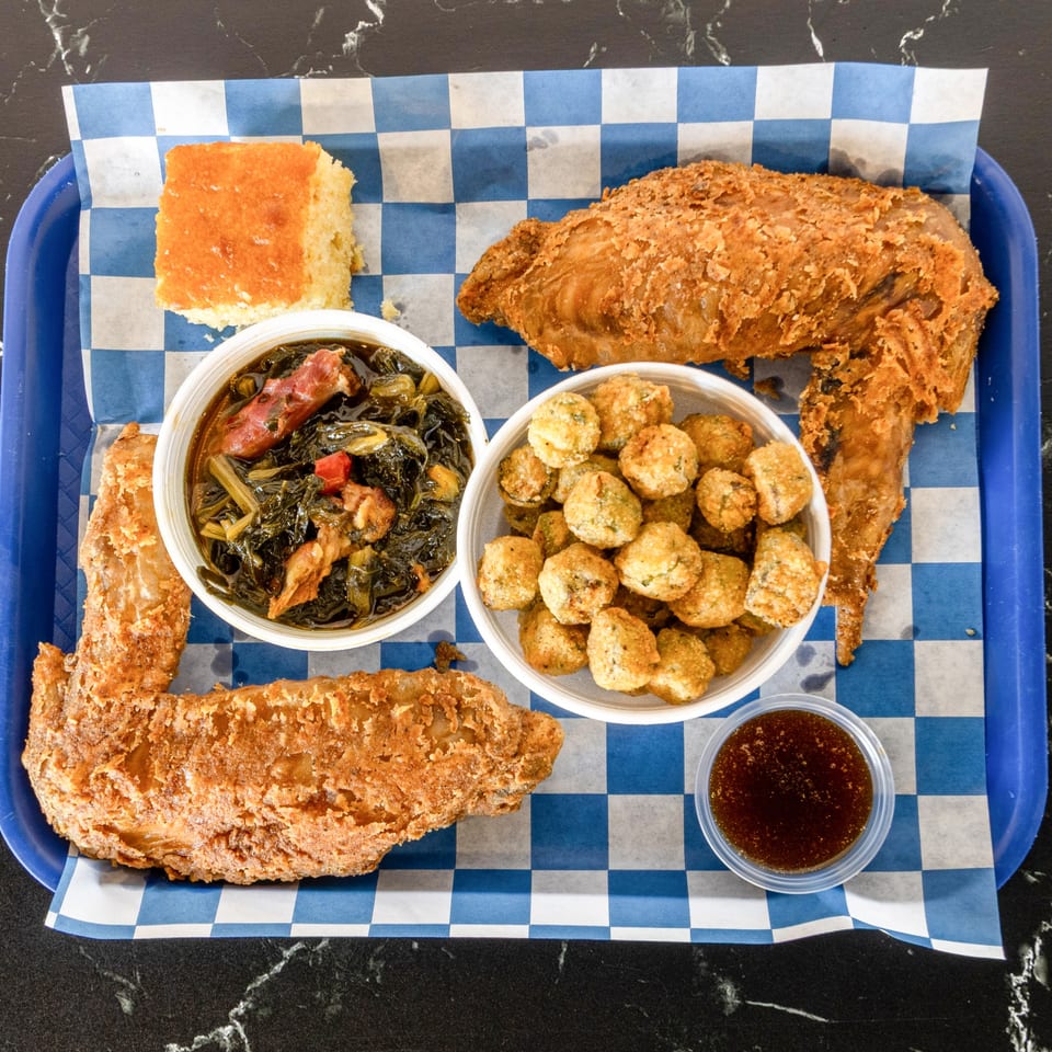 Suthern Cluck fried chicken wings, collard greens, fried okra, cornbread, and dipping sauce on a tray.