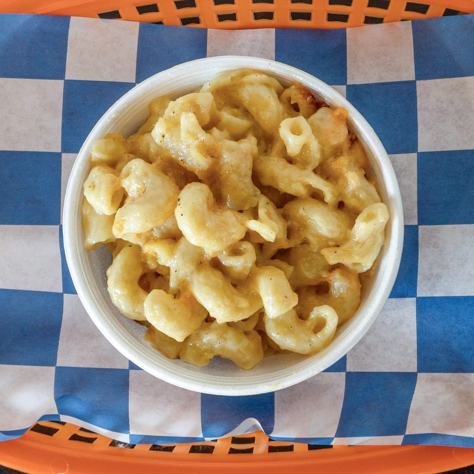 A white bowl of creamy mac and cheese sits on blue and white checkered paper.