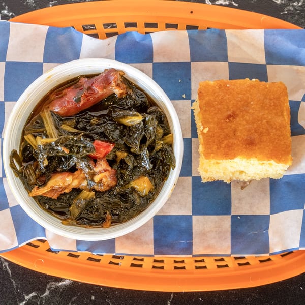 A bowl of Suthern Cluck collard greens with meat and a side of cornbread in a basket.